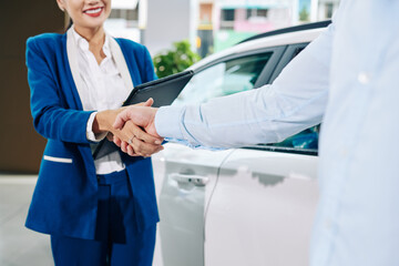 Sales assistant shaking hand of client after he is buying car at dealership