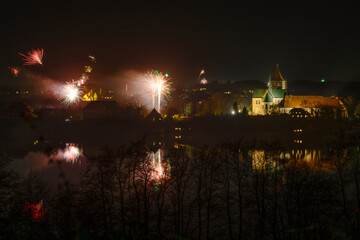 Fototapeta na wymiar New Year fireworks at the Ratzeburg cathedral with reflections in the lake at night, copy space in the dark sky