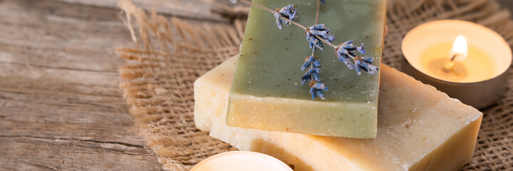 Green and yellow soaps with a scented candle in a romantic setting. Spa concept on wooden background. Advertising banner