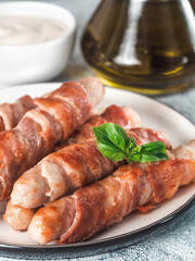 Ready-to-eat pigs sausages wrapped in bacon on plate. Fried savory sausages wrapped in bacon served fresh green basil leaves with sauce on background. Shallow DOF. Copy space for text. Vertical.