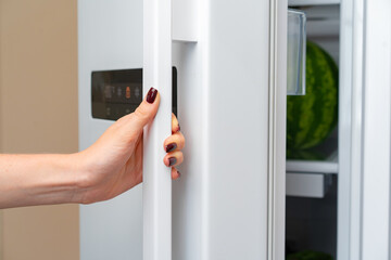 Female hand opens door of a fridge