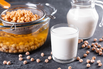 Chickpea vegetarian milk in a jug and glass and raw chickpeas on a table. Lactose free non dairy products.