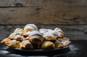 Homemade cookies in the form of bagels with jam filling sprinkled with powdered sugar on a wooden background.
