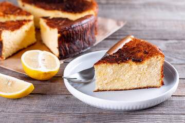 Piece of San Sebastian Basque Cheesecake on the plate on a table with lemon and a cup of tea