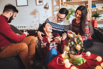Group of friends sitting in nicely decorated house, having fun while celebrating Christmas or New Year