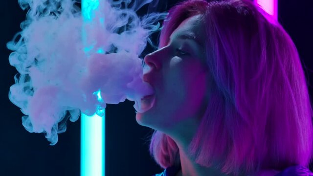 Portrait of a young stylish woman smokes a hookah and blows out puffs of smoke. Close up. Slow motion.