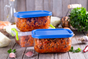 Stewed cabbage in a container on a wooden background for freezing. Frozen food,