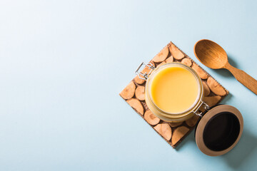 Obraz premium Ghee or clarified butter in jar and wooden spoon on blue background. Top view. Copyspace. Ghee butter have healthy fat and is a common cooking ingredient in many of the Indian food