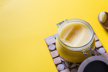 Ghee or clarified butter in jar and wooden spoon on yellow background. Top view. Copyspace. Ghee butter have healthy fat and is a common cooking ingredient in many of the Indian food