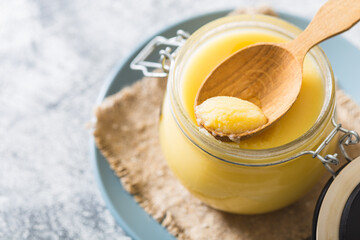 Ghee or clarified butter in jar and wooden spoon on gray table. Top view. Copyspace. Ghee butter have healthy fat and is a common cooking ingredient in many of the Indian food