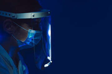 Fototapeta na wymiar woman doctor with face shield and mask side view on dark blue background