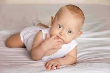 A charming boy licks his fingers while lying on his stomach. The view of a serious person