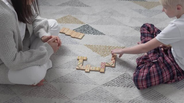 Mom and son play in wooden dominoes at home on the floor in winter.