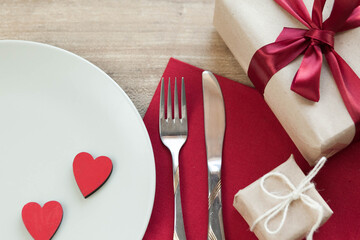 Festive table setting for Valentine's Day with plate, gift boxex, fork, knife and hearts on a wooden table. Love anniversary.