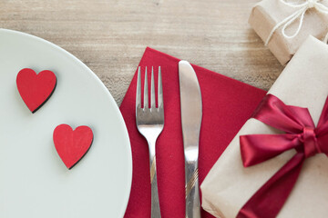 Festive table setting for Valentine's Day with plate, gift boxex, fork, knife and hearts on a wooden table. Love anniversary.