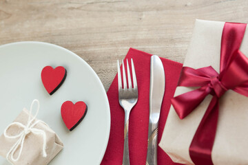 Festive table setting for Valentine's Day with plate, gift boxex, fork, knife and hearts on a wooden table. Love anniversary.