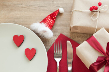 Festive table setting for Valentine's Day with plate, gift boxes, fork, knife and hearts on a wooden table. 