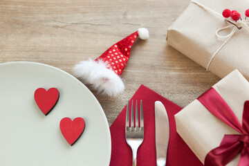 Festive table setting for Valentine's Day with plate, gift boxes, fork, knife and hearts on a wooden table. 