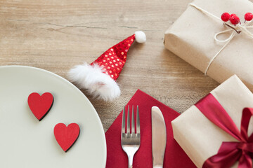 Festive table setting for Valentine's Day with plate, gift boxes, fork, knife and hearts on a wooden table. 