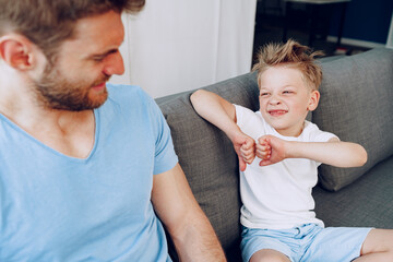 Son showing thumbs down while sitting on sofa with his father