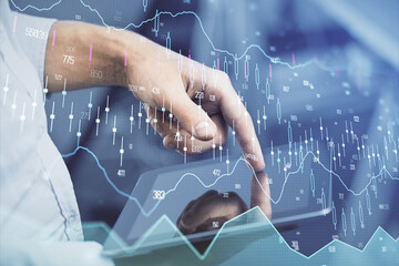 Double exposure of man's hands holding and using a digital device and forex graph drawing. Financial market concept.