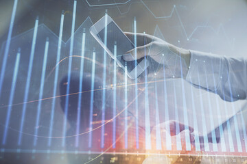 Double exposure of man's hands holding and using a digital device and forex graph drawing. Financial market concept.