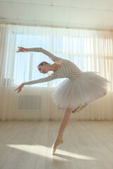 Beautiful ballerina in body and white tutu is training in a dance class. Young flexible dancer posing in pointe shoes.