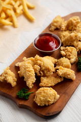 Homemade Popcorn Chicken on a rustic wooden board on a white wooden table, side view. Close-up.