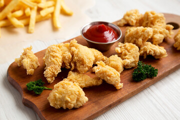 Homemade Popcorn Chicken on a rustic wooden board on a white wooden background, low angle view.