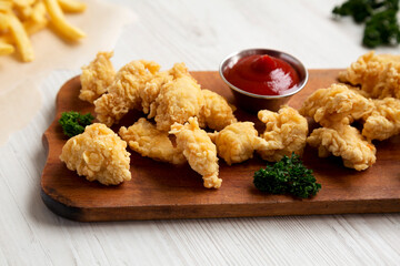 Homemade Popcorn Chicken on a rustic wooden board on a white wooden background, side view. Close-up.