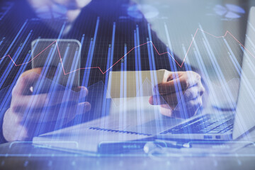 Double exposure of man's hands holding and using a phone and financial graph drawing. Analysis concept.