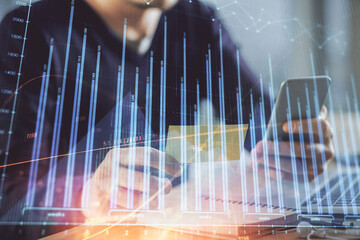 Double exposure of man's hands holding and using a phone and financial graph drawing. Analysis concept.