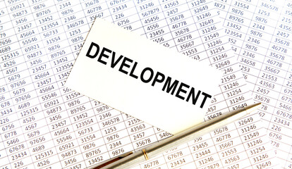 On the business card the text OF DEVELOPMENT, next to the pen, the background are reports.