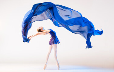 Elegant ballerina in pointes dances with developing blue cloth on white background