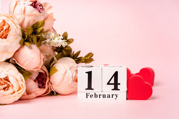 Flower composition with hearts for February 14 on a pink background with a wooden calendar
