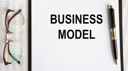 On the tablet for writing the text BUSINESS MODEL, next to glasses, pen, reports.