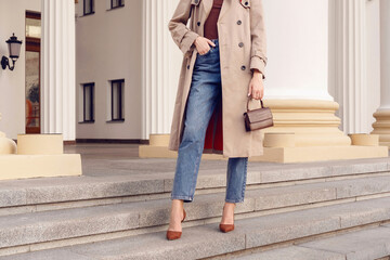 Fashion model woman in beige coat and jeans with brown mini bag on the stairs