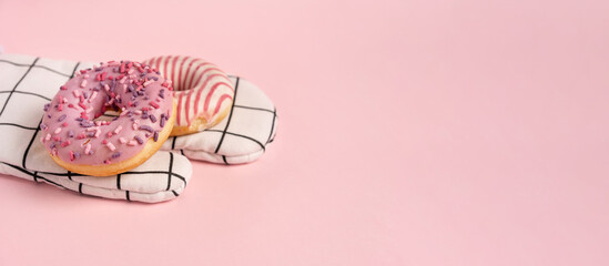 Donuts decorated with icing and topping lie on the chef's glove on a pink background top view copy