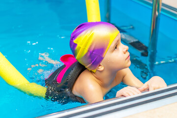 A small child with a life jacket on his chest is learning to swim in an indoor pool.
