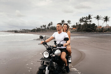 Obraz premium Young couple riding motorcycle on the beach, outdoor portrait, blonde girl, travel together, ocean, sea