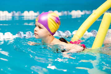 A little boy with a life jacket on his chest learns to swim in an indoor pool.