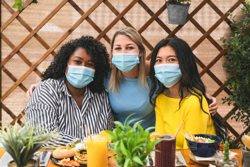 Multiracial friends wearing face mask while having healthy lunch in coffee brunch bar during corona...