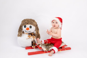 little baby girl sitting on a red sled in a Santa hat on a white isolated background with a snowman, happy new year 2021, space for text