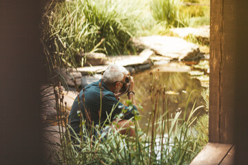 Elderly man taking pictures of water as a hobby. Leisure in old age. Relaxing at home in the garden alone.