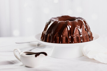 Dark chocolate cake covered with icing on a white stand. Selective focus.