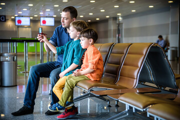 Mother and two brother boy son pointing at taking off airplanes through window glass in airport while waiting for their flight