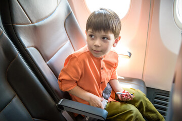 Child in airplane. Kid in air plane sitting in window seat. Flight entertainment for kids. Traveling with young children. Kids fly and travel. Family summer vacation. Little boy with toy in airplane