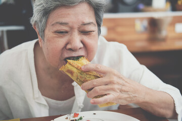 old asian elderly senior elder woman eating vegan wrap with quinoa, black bean, mango, cashew nut,...