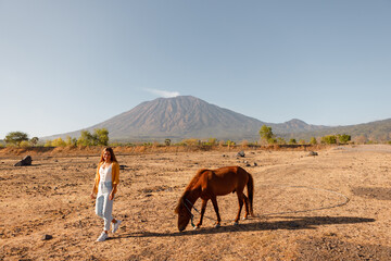 Woman rider walk and smiles next to the horse, mountain on background