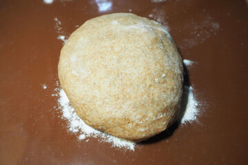 a raw round brown dough made of rye flour water butter and egg lies on a brown silicone Mat side view